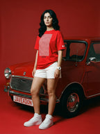 Woman in red Javeadon tee and white shorts leaning on vintage red car, bold streetwear style