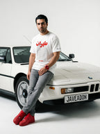 Man in white Persian graphic tee and red sneakers leaning on white BMW, Javeadon streetwear style