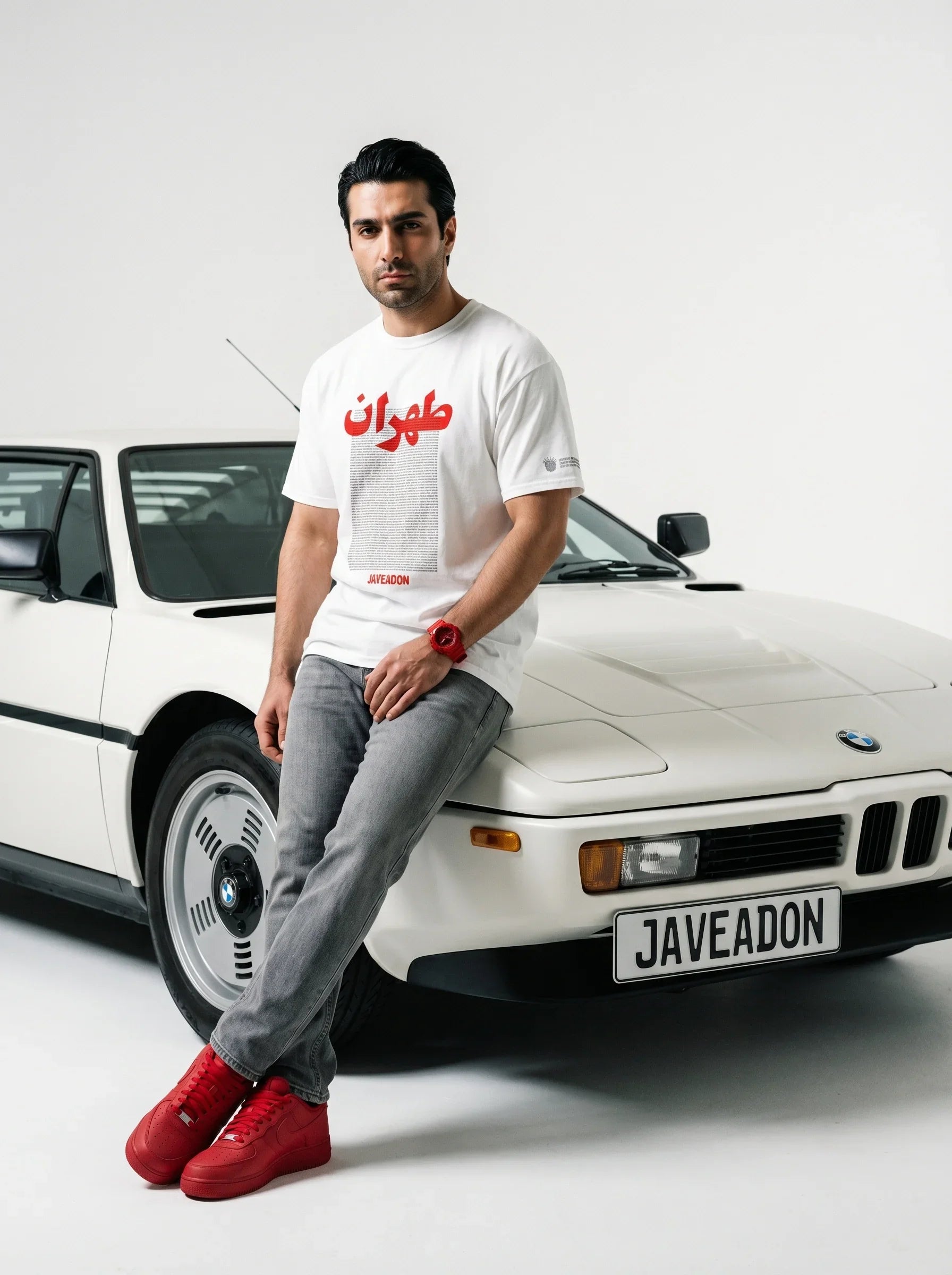 Man in white Persian graphic tee and red sneakers leaning on white BMW, Javeadon streetwear style