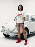 Woman in white Persian graphic tee, red sneakers, standing by white vintage car, Javeadon brand
