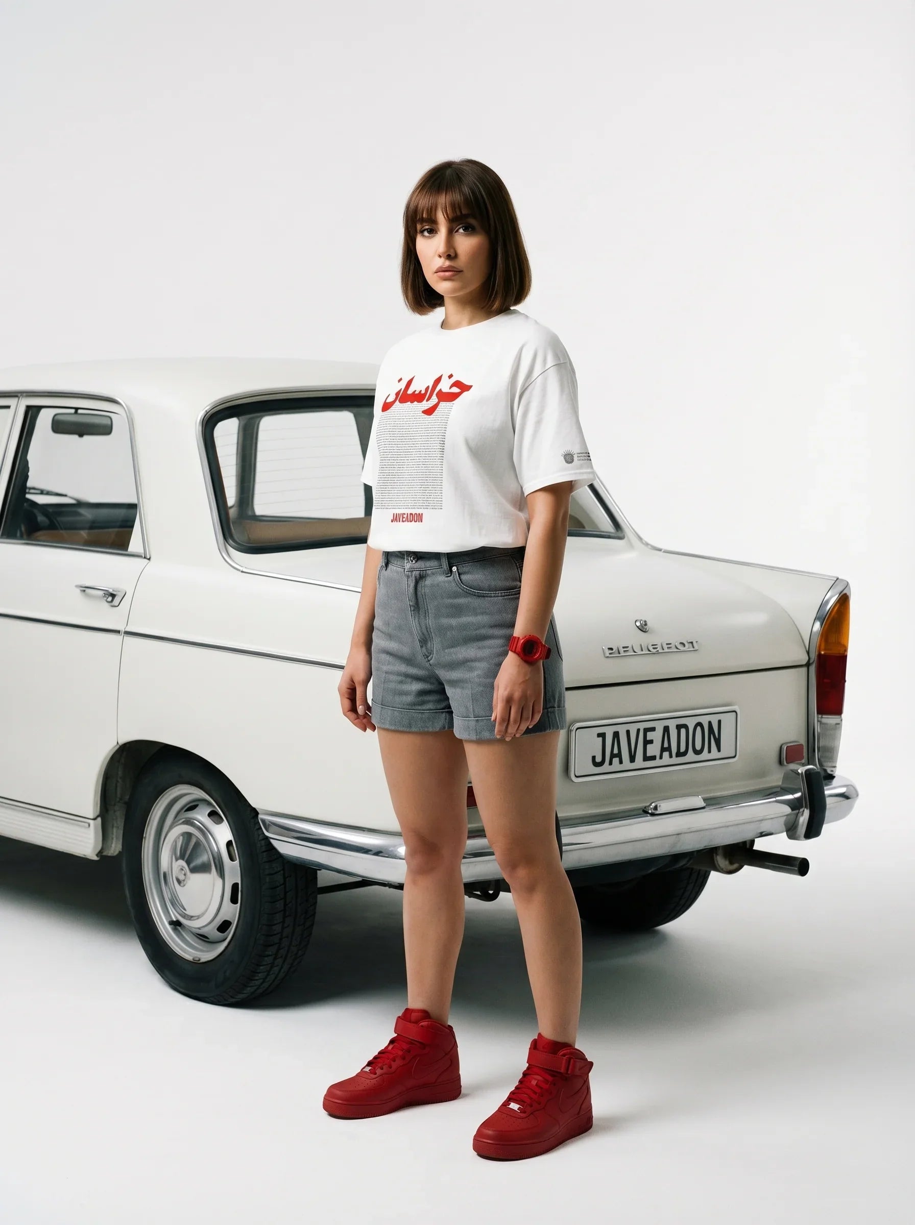 Woman in white Persian-themed tee, denim shorts, red sneakers, standing by vintage car