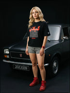Woman in black Persian graphic tee, denim shorts, red sneakers, standing by classic black Fiat car