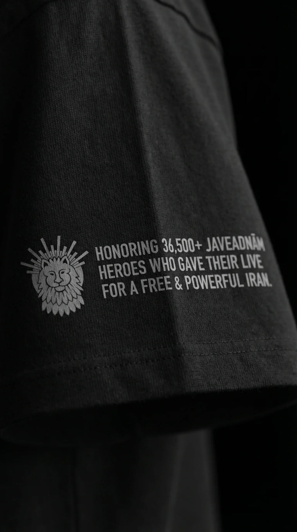 Black t-shirt sleeve with lion emblem and text honoring 36,500+ Javeadnām heroes for a free Iran