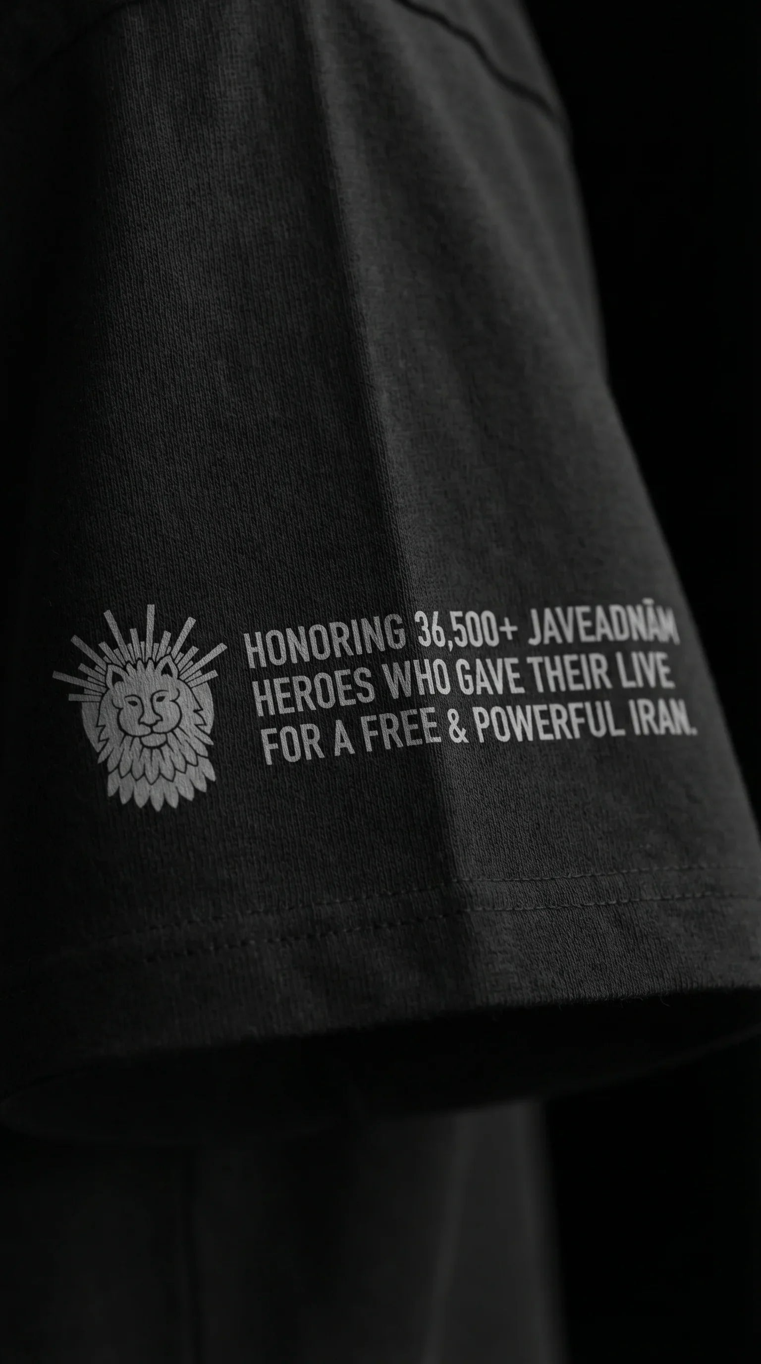 Black t-shirt sleeve with lion emblem and text honoring 36,500+ Javeadnām heroes for a free Iran