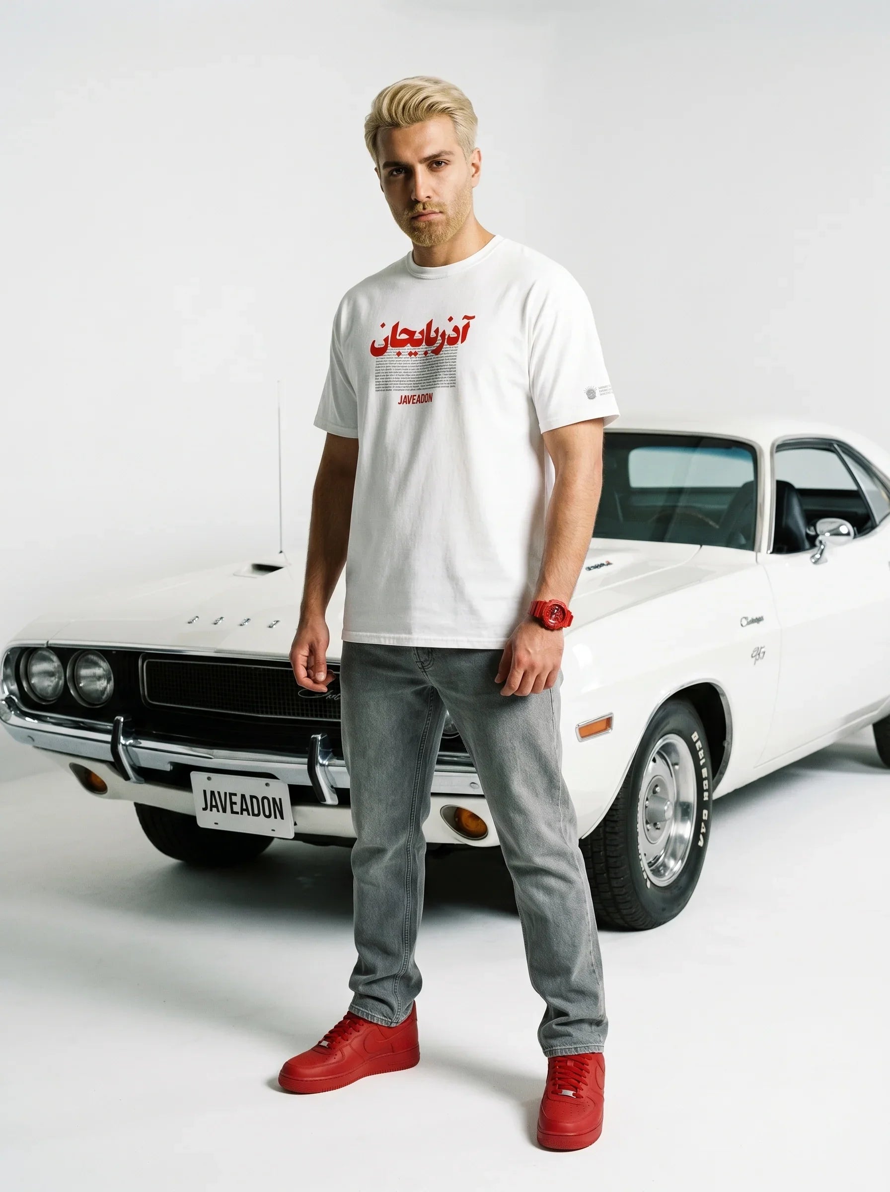 Man in white Persian graphic tee, grey jeans, red sneakers, standing by classic white muscle car