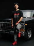 Man in black Persian streetwear tee with red graphics, leaning on classic Ford truck, bold red sneakers