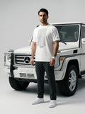 Man in white Javeadon t-shirt standing beside white luxury SUV, showcasing Persian-inspired streetwear.