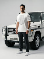Man in white Javeadon t-shirt standing beside white luxury SUV, showcasing Persian-inspired streetwear.