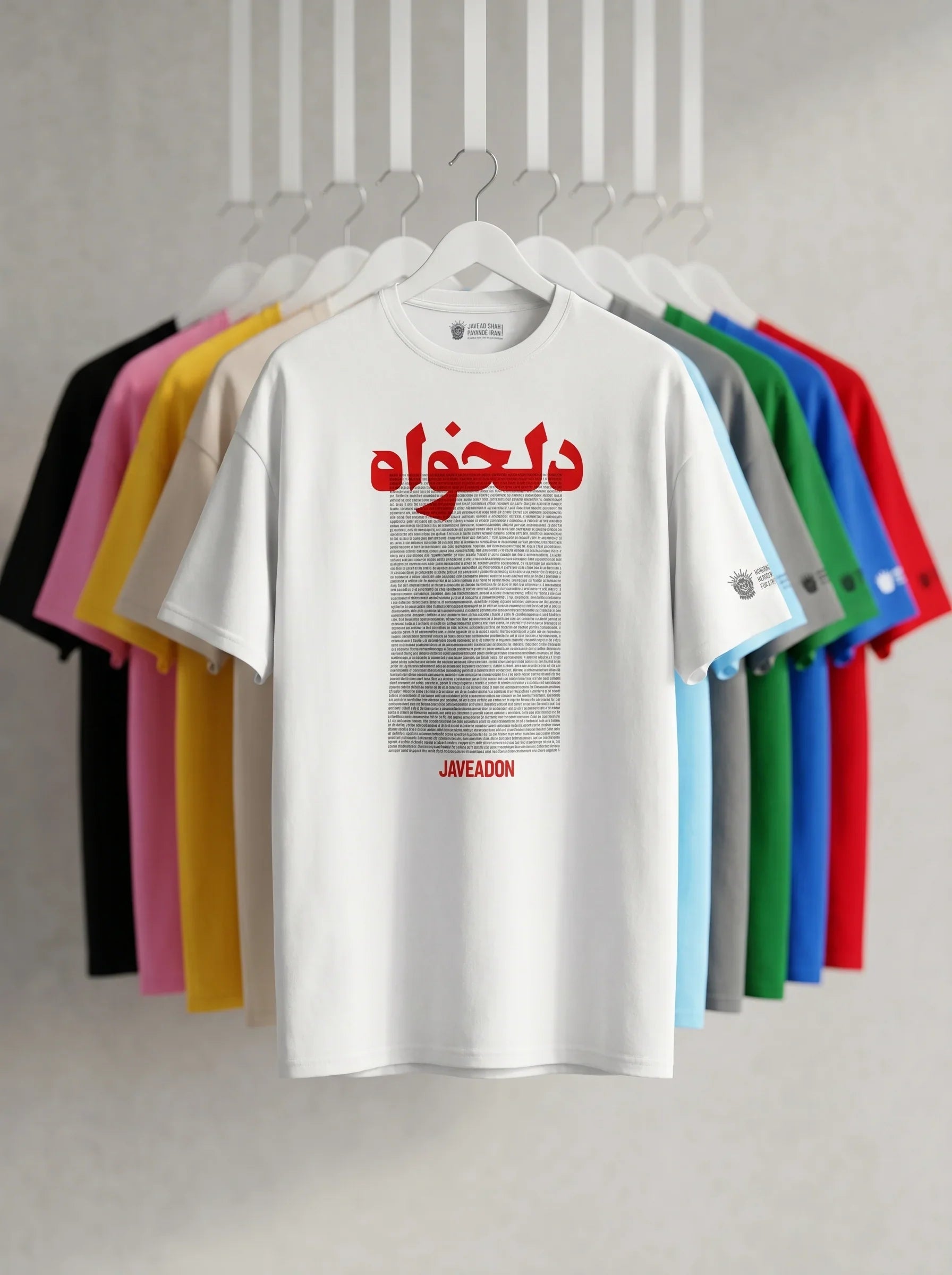 White t-shirt with bold red Persian text and 'JAVEADON' print, displayed with colorful shirts on hangers.