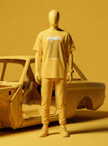 Mannequin in yellow streetwear with Persian text, styled beside a vintage car frame.