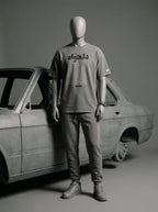 Mannequin wearing gray streetwear tee with Persian text, paired with joggers, beside vintage car.