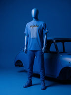 Blue mannequin wearing Persian-inspired streetwear tee with text graphic, styled with joggers and sneakers beside vintage car