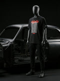 Black mannequin wearing Persian-themed streetwear tee with red text, styled with black joggers and sneakers near car frame