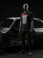 Black mannequin wearing Persian-themed streetwear tee with red text, styled with black joggers and sneakers near car frame