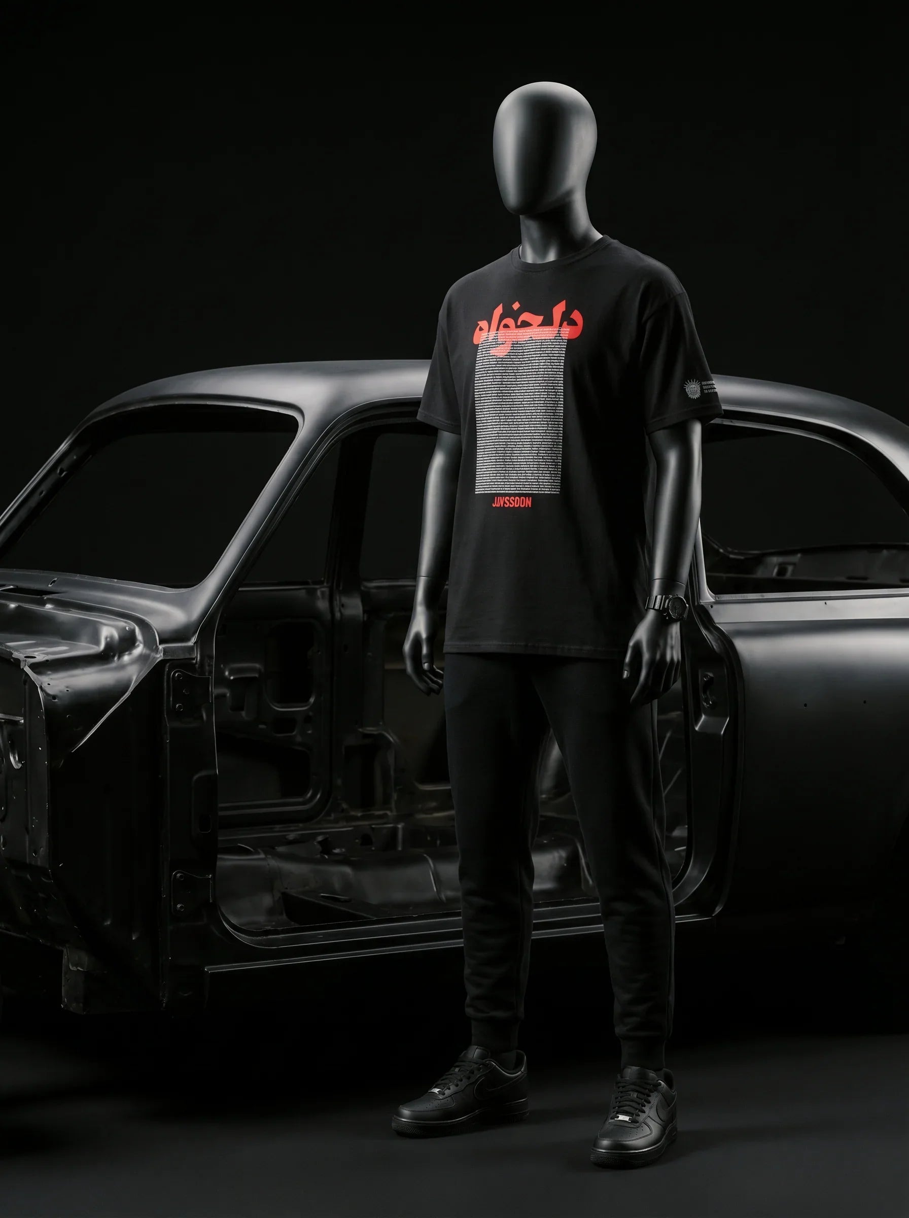 Black mannequin wearing Persian-themed streetwear tee with red text, styled with black joggers and sneakers near car frame