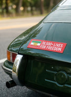 Red sticker on green car trunk with Lion & Sun flag and text '36,500+ Lives For Freedom'