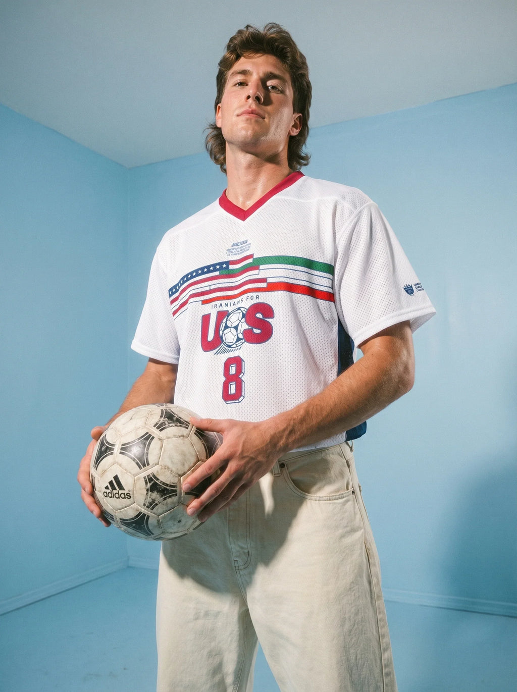 Man holding soccer ball in vintage US soccer jersey with 'Iranians for US' graphic, retro streetwear style